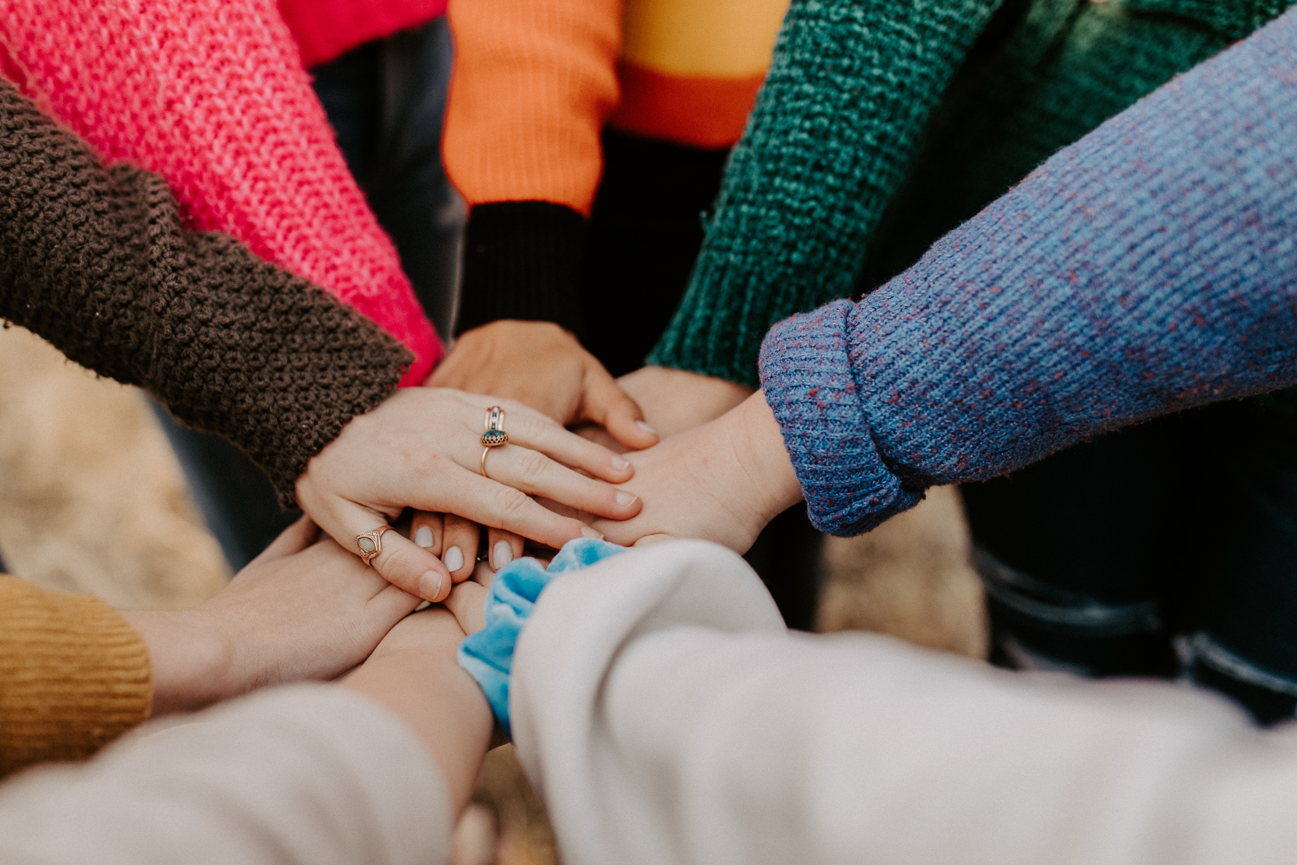 A group of hands, one on top of another in a circle, symbolizing community, cooperation, and teamwork