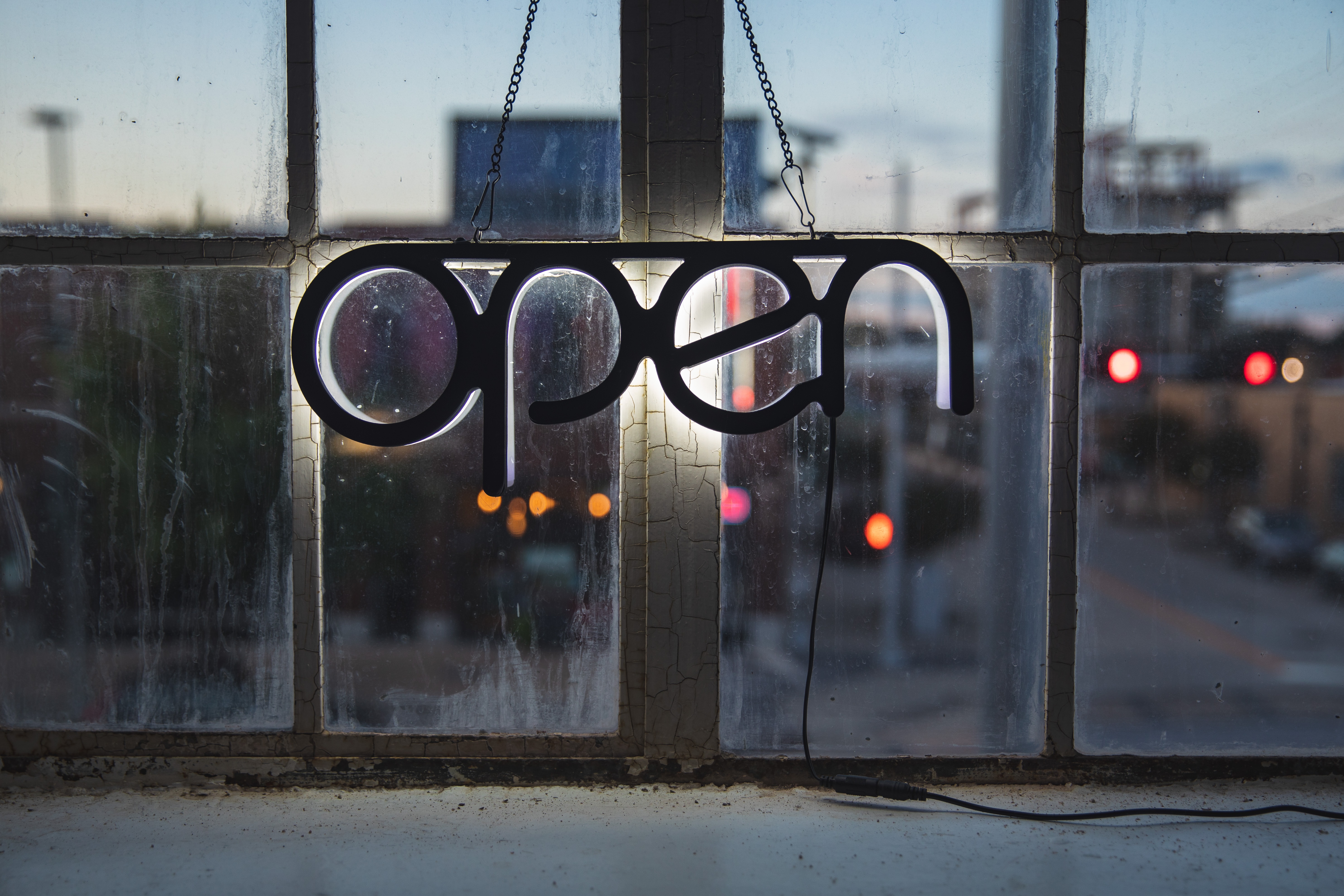 Ah open sign gently backlighting an old window in an industrial setting at dawn/dusk