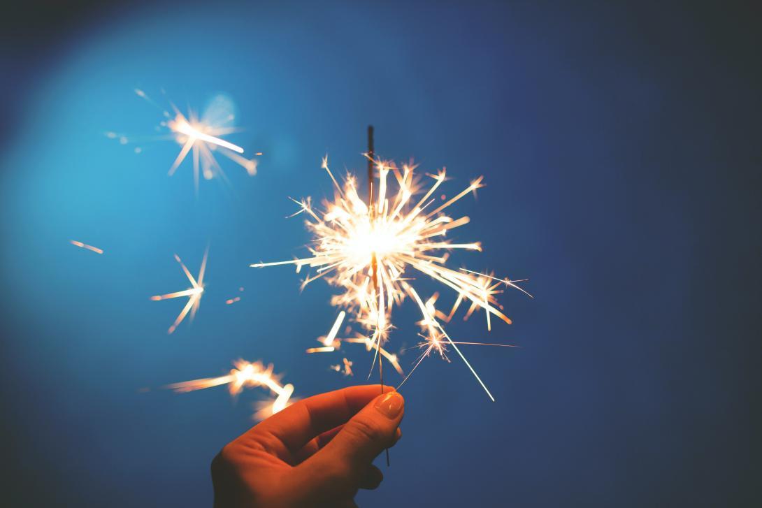 A sparkler held up the night sky. Tight cropped to just the fingers and sparks